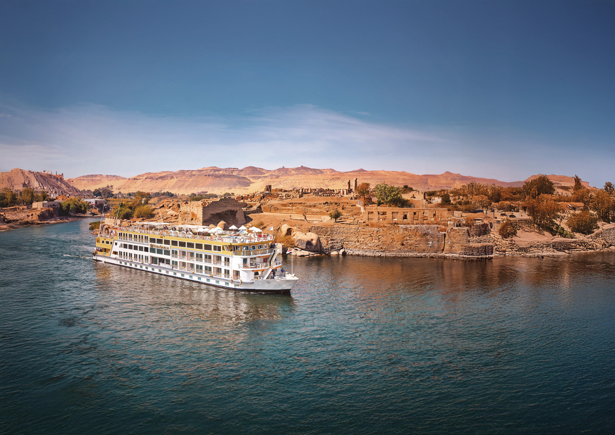 A luxurious river cruise ship with distinctive yellow and white livery navigates the Nile River
