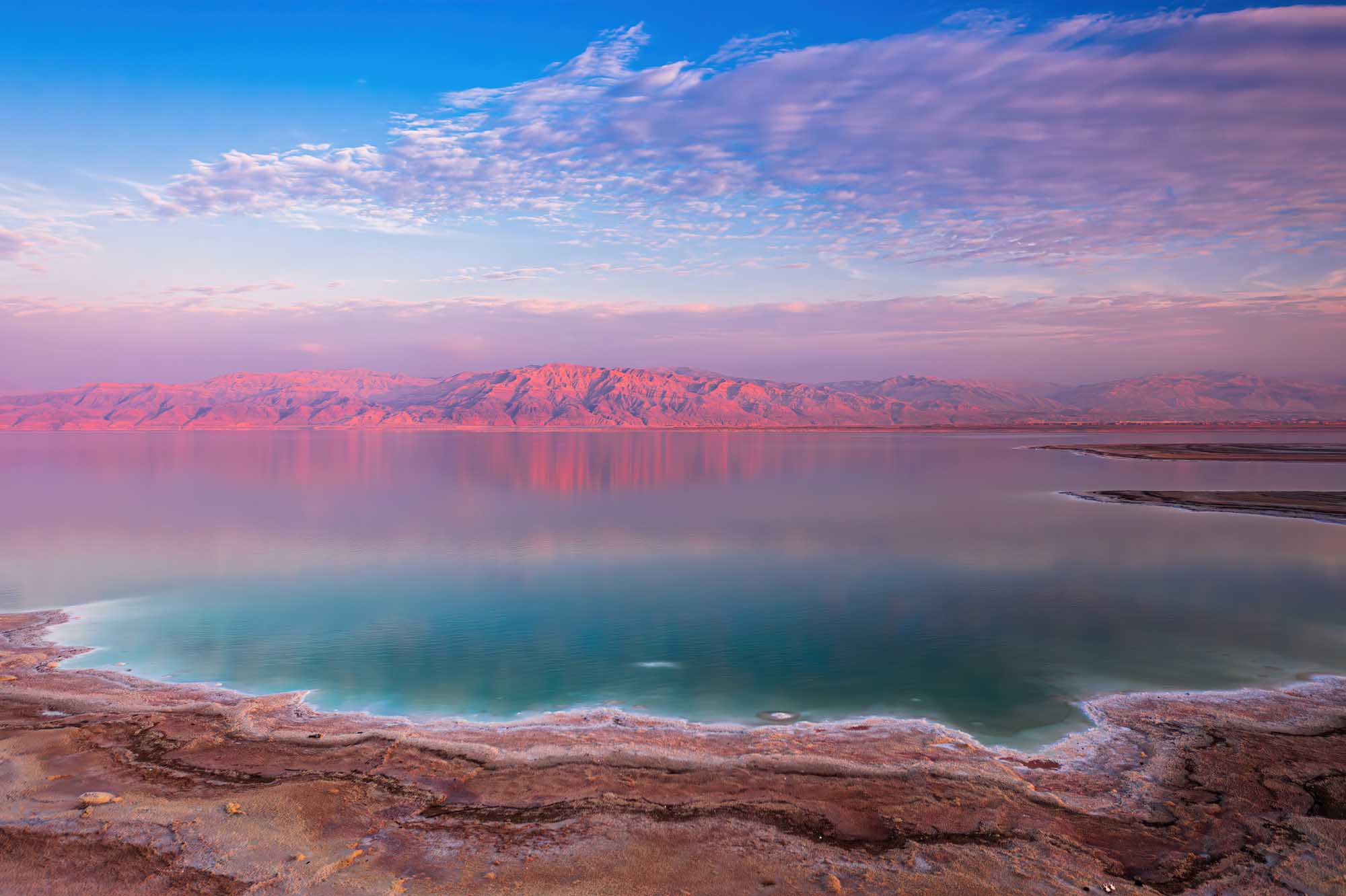 Dead Sea at Sunset with Mountain Reflections A stunning panoramic view of the Dead Sea at sunset, with vibrant pink and turquoise hues