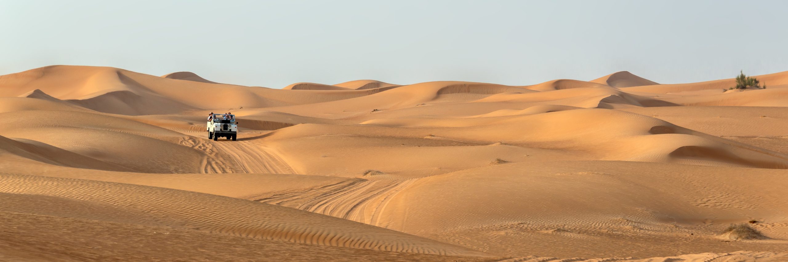 A white four-wheel-drive vehicle navigates through vast, undulating sand dunes in a desert
