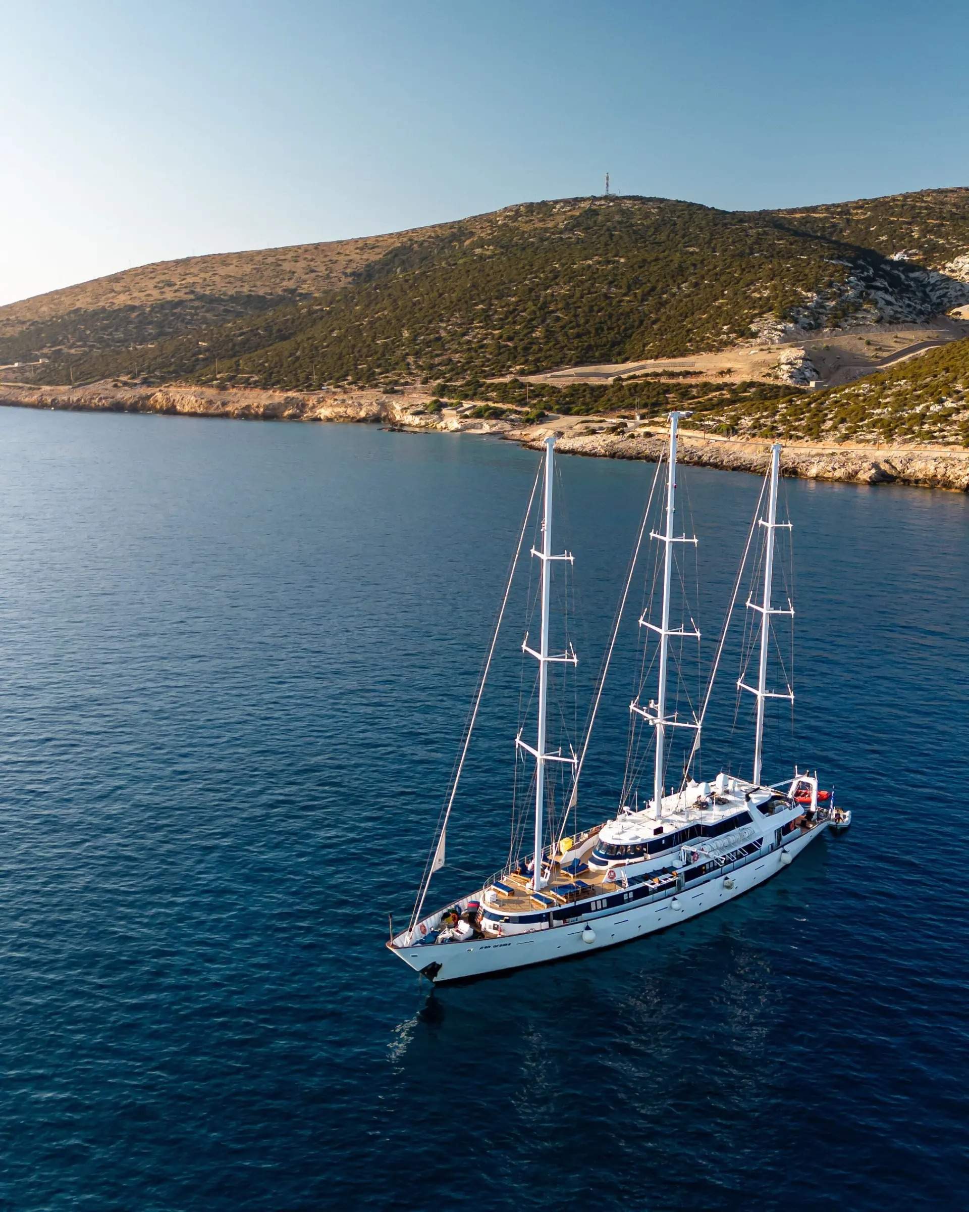 A elegant multi-masted sailing yacht with white hull and full rigging is anchored in crystal-clear