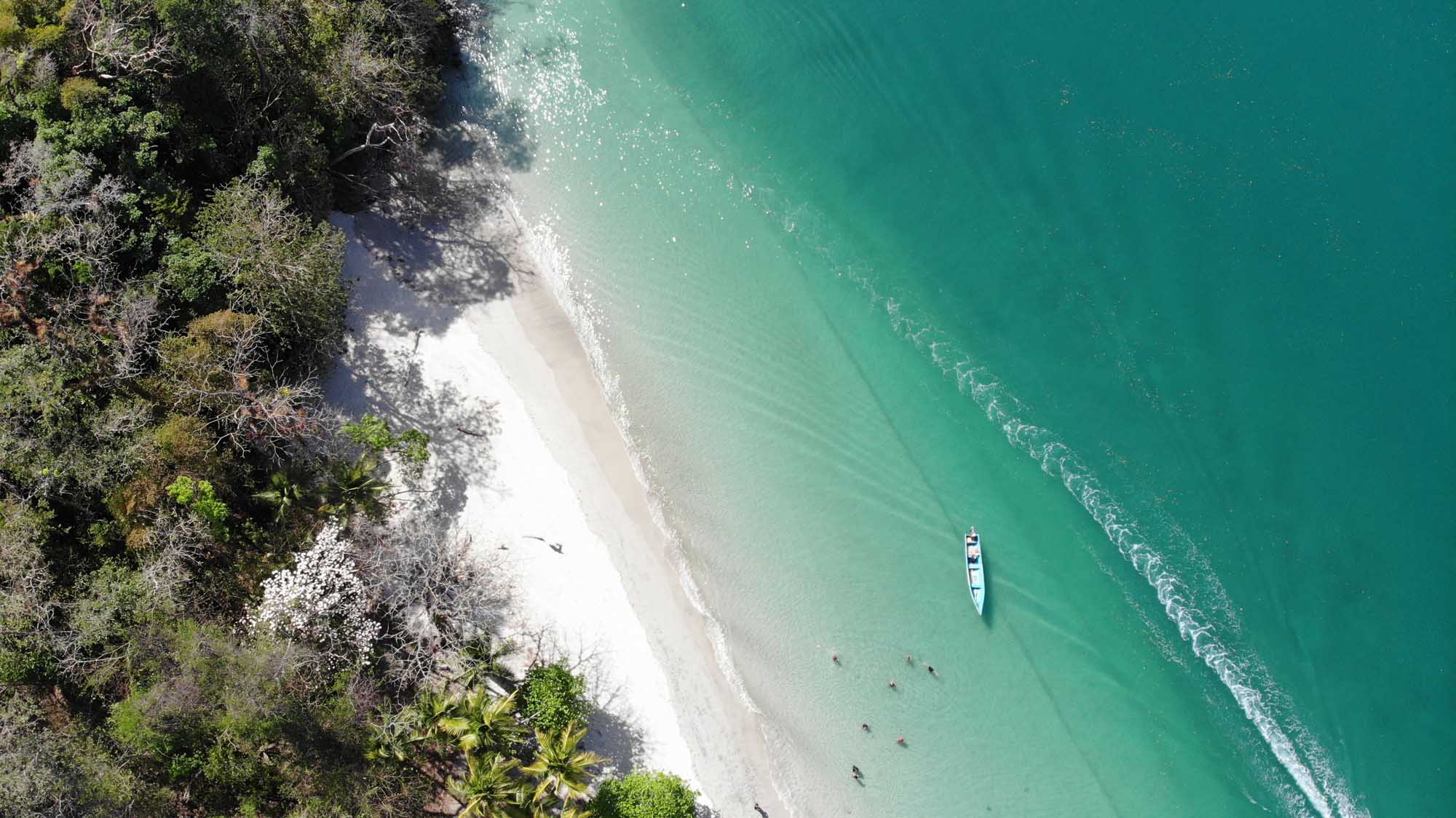 Tropical Beach Cove with Anchored Boat An aerial view of a pristine tropical beach with turquoise waters, white sand, and dense green